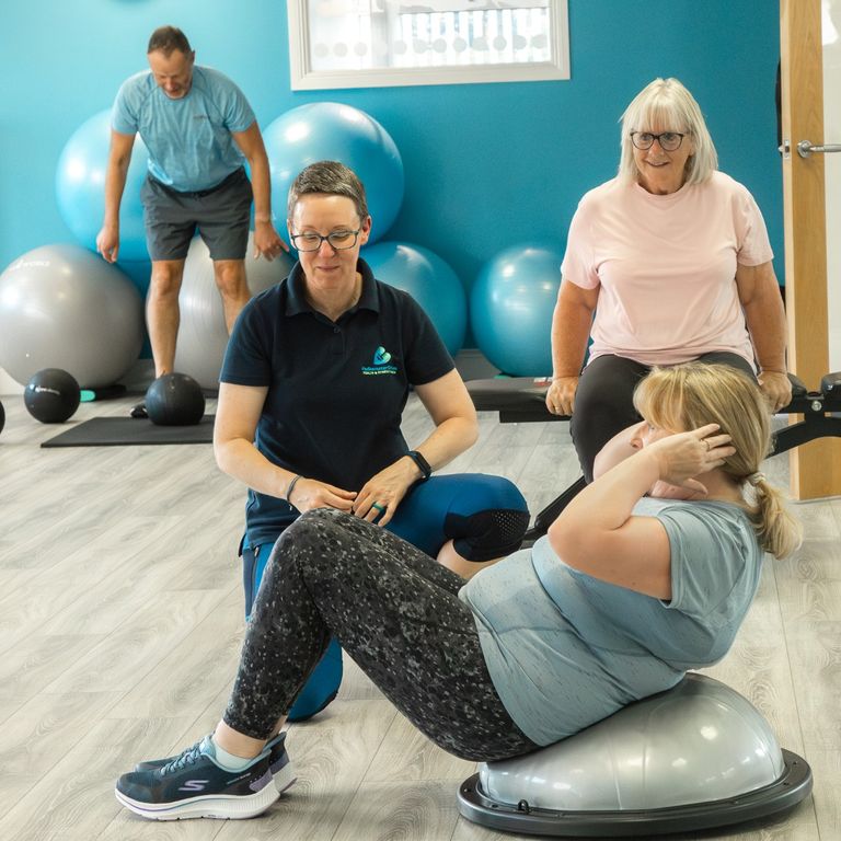 Pauline is kneeling on the floor  instructing a client to do an ab crunch.