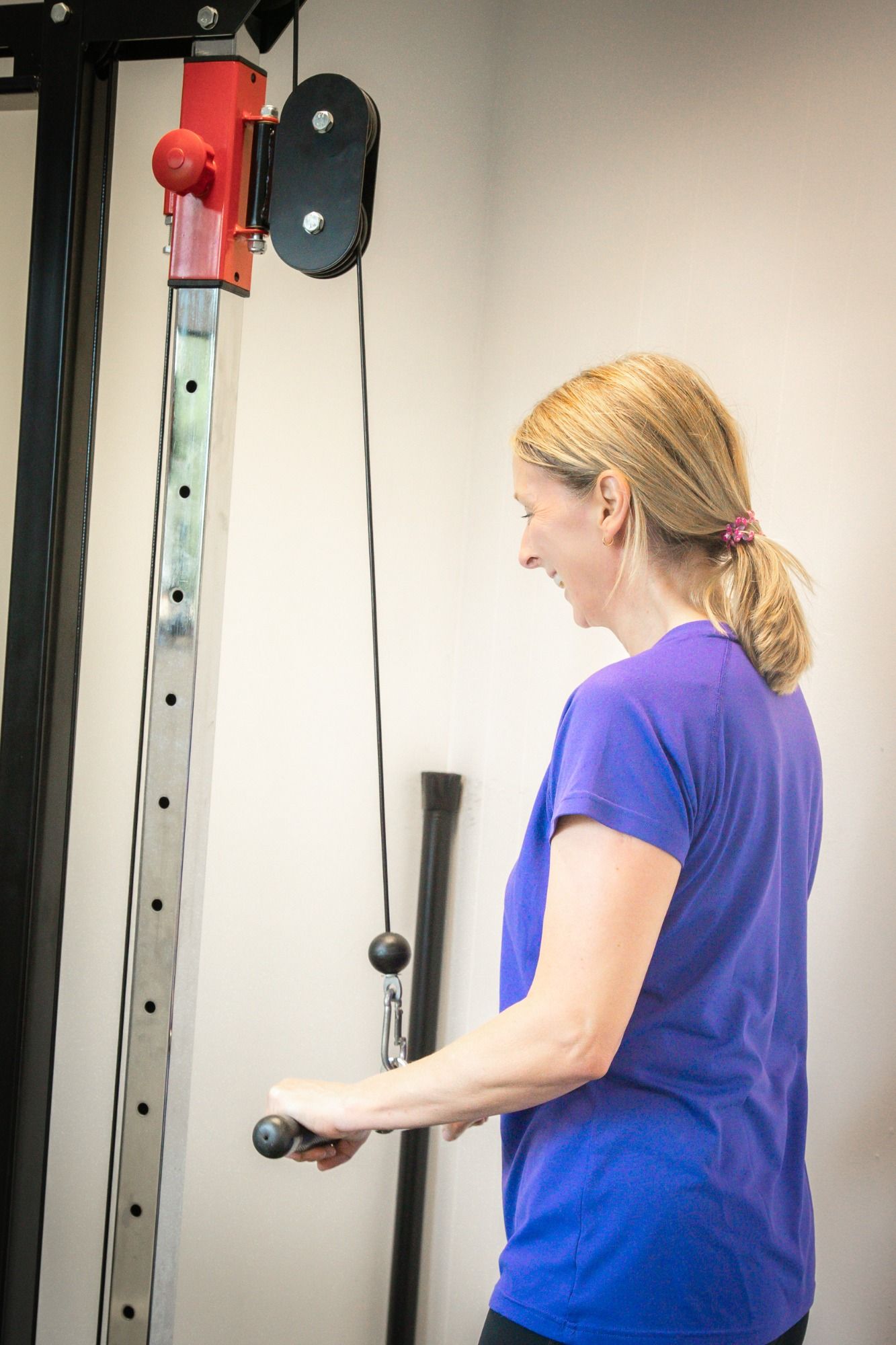 A Personal Training client is performing a tricep exercise on a cable machine. The client is smiling and enjoying the exercise.