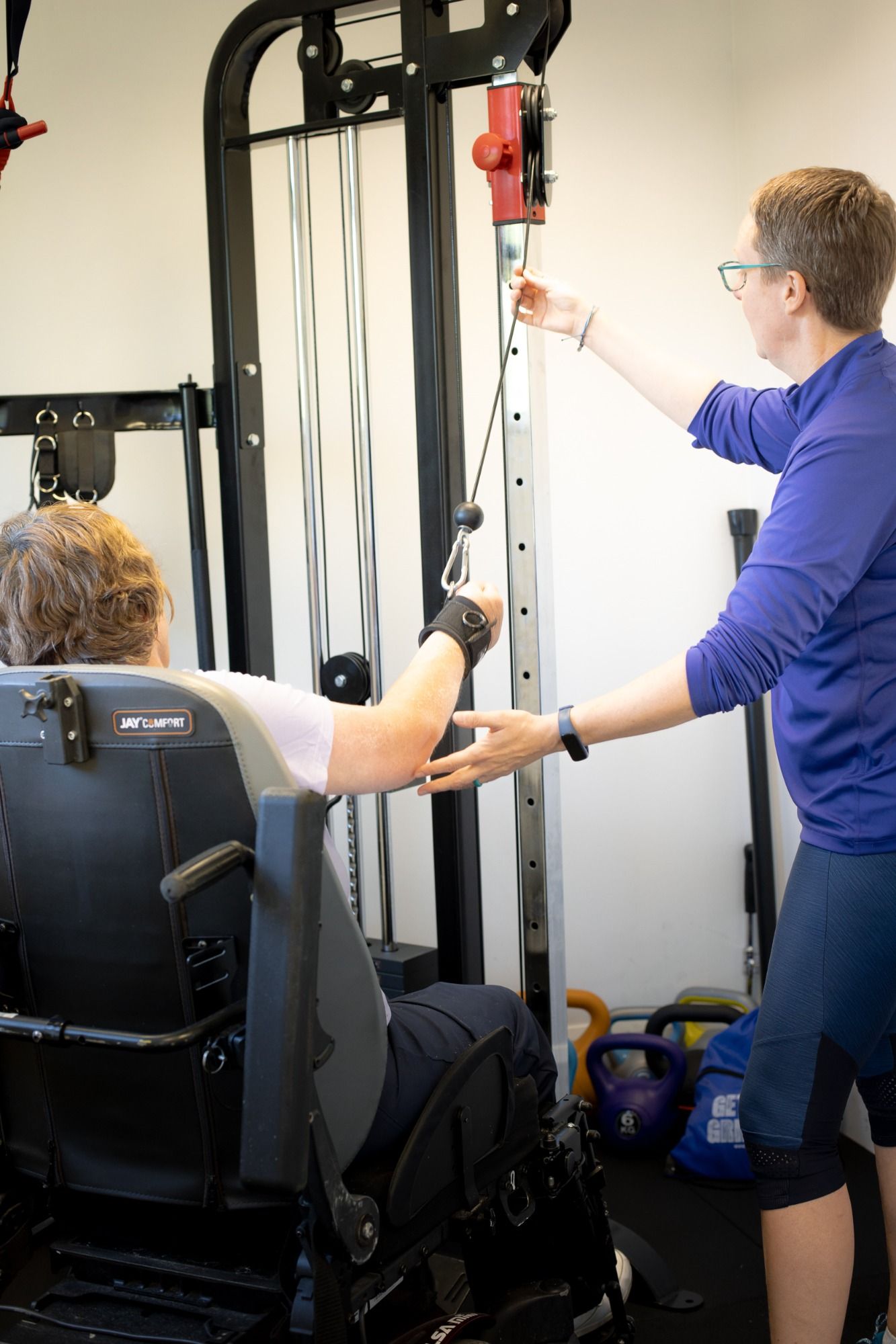 Pauline is assisting a wheelchair client to use a cable machine and the client is using Active Hands grip device.