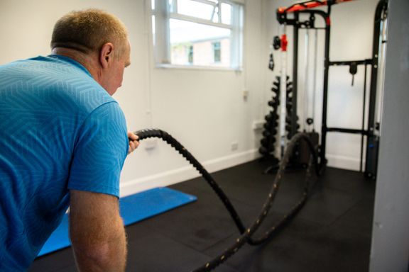 Male client using battle ropes in workout studio.